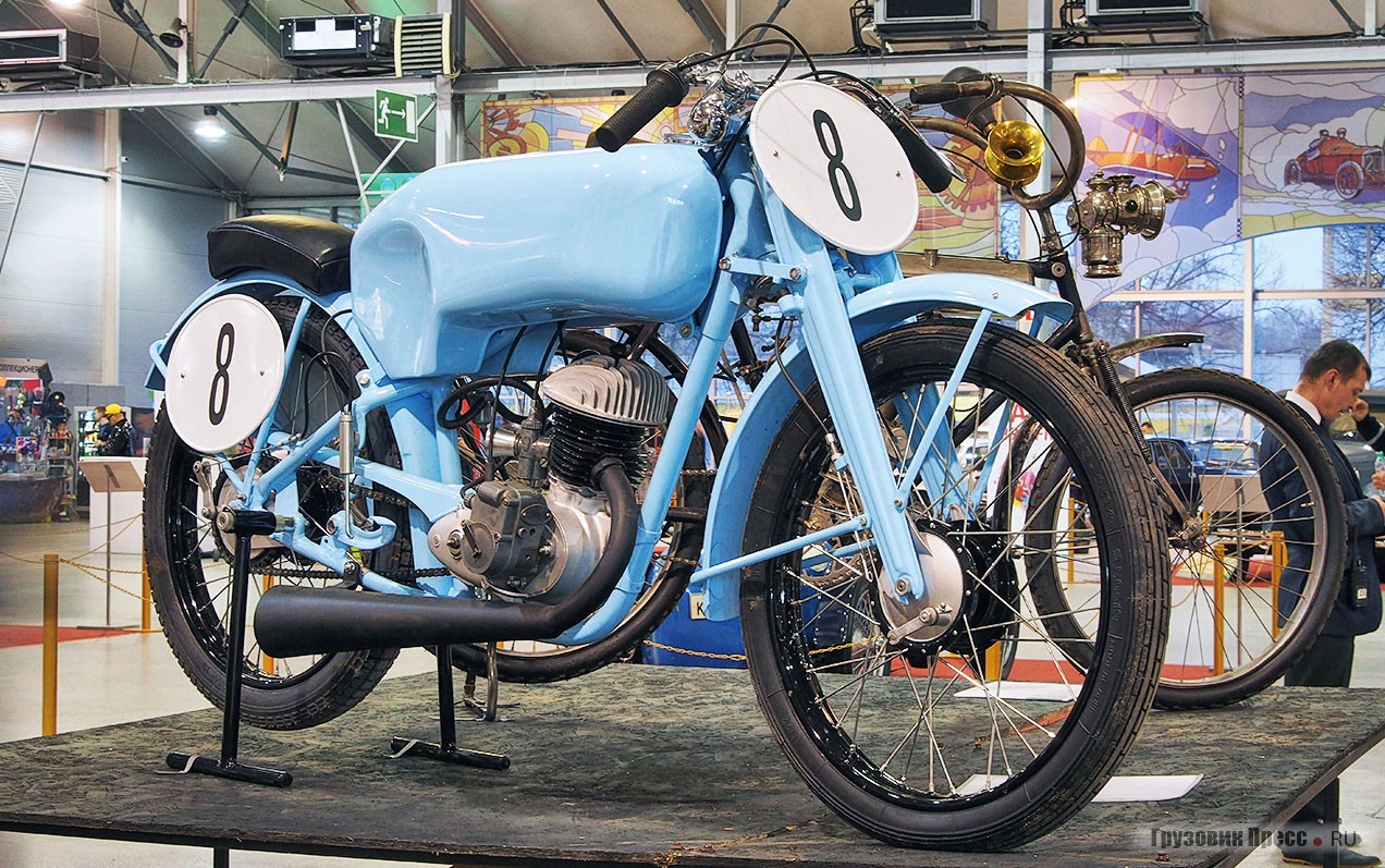 «Мотоциклетный спорт – витрина ДОСААФ!». [b]Гоночный мотоцикл М-1Е[/b] производства Московского мотоциклетного завода (1950 год) принадлежал чемпиону Москвы и РСФСР, спортсмену общества «Торпедо» Виктору Ивановичу Соколову. Отличия машины от серийной «макаки»: два карбюратора, 7,5 л.с., зажигание от магнето, ёмкий бак, двухсторонние тормоза. Выставлен известным знатоком велосипедов Андреем Мятиевым